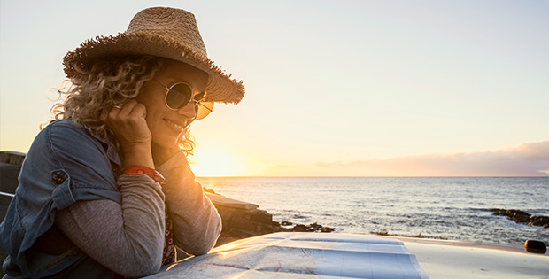 Frau mit Strohhut sitzt lachend am Meer
